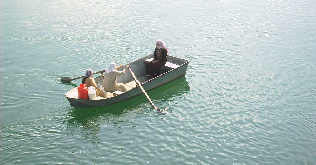 Imagem de três mulhares usando turbantes dentro de um pequeno barco no meio do mar