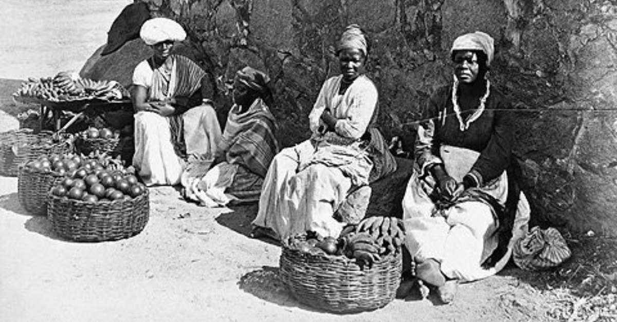 Quatro mulheres negras sentadas com cestos de frutas à frente